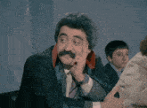 a man with a mustache is wearing a black suit and tie