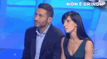 a man in a suit and a woman in a green dress are sitting next to each other on a blue background .