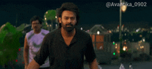 a man with a beard is standing in front of a city at night with the hashtag @avantika_0902