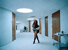 a woman is standing in a hallway with a man sitting in a chair behind her