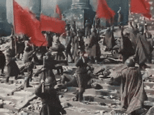 a group of soldiers holding red flags are standing in a ruined city .