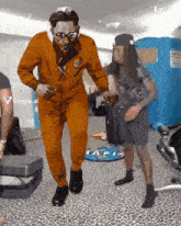 a man in an orange suit is dancing in a room with a sign that says viggle.ai on it