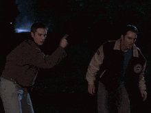 a man wearing a varsity jacket with the letter e on it stands next to another man