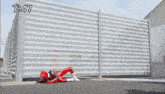 a red superhero is laying on the ground in front of a fence with the time 7:47 on the bottom