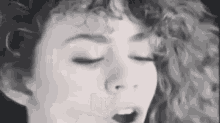 a black and white photo of a woman with curly hair singing with her eyes closed .