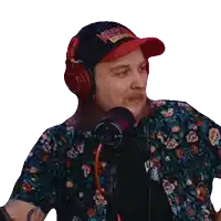 a man wearing a hat and headphones is talking into a microphone while wearing a floral shirt .
