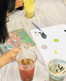 a woman is painting a picture with a straw in a glass