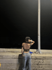 a woman in a leopard print top and jeans is standing next to a pole in the dark