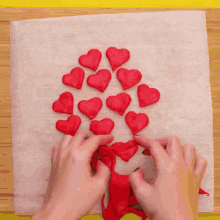 a person is making a tree of red hearts on a piece of wax paper