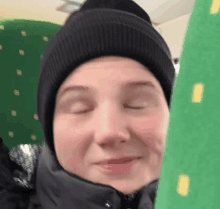 a person wearing a beanie and a jacket is sitting on a green seat with their eyes closed .