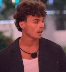 a young man with curly hair is wearing a black jacket and a black necklace .