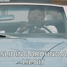 a man is driving a car with the words " sliding around a lil bit " on the hood