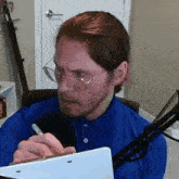 a man with glasses is writing on a clipboard with a pen