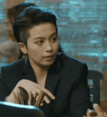 a woman in a black suit is sitting at a table holding chopsticks