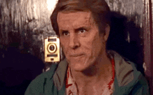 a man in a green jacket is sitting in front of a door and making a funny face .