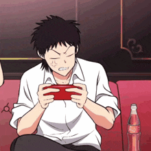 a man sitting on a couch playing a video game next to a coca cola bottle