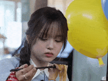 a girl is eating noodles with chopsticks and a yellow balloon in the background