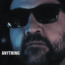 a man with a beard is wearing sunglasses and the word anything is above his head