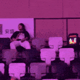 a woman sits in a stadium watching a game with a sign that says ae on it