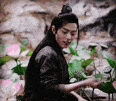 a man with long black hair is standing in a field of flowers