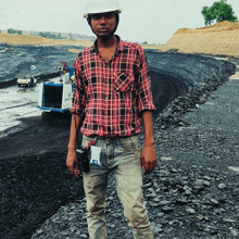 a man wearing a hard hat and plaid shirt stands in front of a large pile of coal