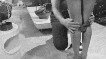 a black and white photo of a man kneeling down next to a woman 's legs .
