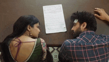 a man and woman sit at a table with a piece of paper on the wall