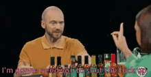 a man is talking to a woman while holding a bottle of hot sauce in front of him