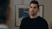 a man in a black shirt is standing in front of a framed picture on the wall .