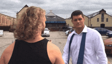 a man in a white shirt and suspenders talks to a woman in a black top