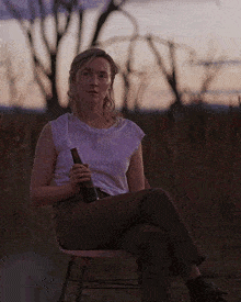 a woman sits in a chair with her eyes closed holding a bottle of beer