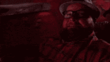 a man with a beard and glasses is wearing a hat and a plaid shirt .
