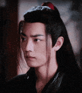 a man with long black hair has a red ponytail