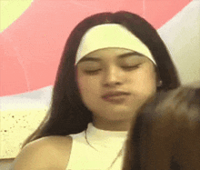 a woman wearing a headband and a white tank top is looking at the camera .