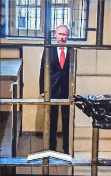 a man in a suit and red tie is behind a fence