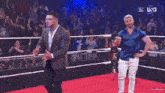 two men are standing on a red carpet in a wrestling ring with a crowd in the background