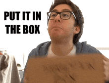 a man wearing glasses is holding a cardboard box with the words put it in the box behind him