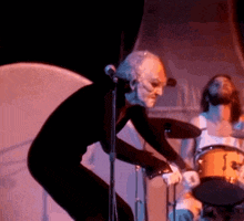 a man is singing into a microphone while another man plays drums