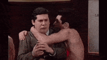 two men are standing next to each other in a room . one of the men is without a shirt on .