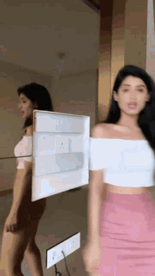 a woman in a pink skirt is standing in front of a mirror holding a white box