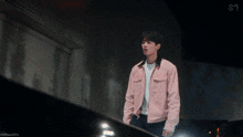 a man in a pink jacket is standing in front of a wall with the letter s on it