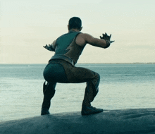 a man in a superhero costume squats on a rock near the ocean