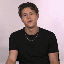 a young man with curly hair wearing a black shirt and a silver chain around his neck