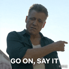 a man pointing at something with the words go on say it written below him