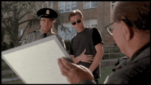 a man in sunglasses looks at a piece of paper while two men in uniform look on