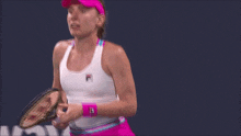 a woman holding a tennis racquet wearing a white tank top with a fila logo on it