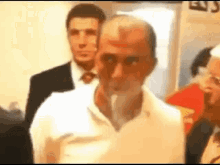 a man in a white shirt is smoking a cigarette in a room with other people .