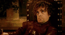 a man with curly hair is sitting in a chair holding a glass of wine .