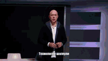 a bald man in a suit stands in front of a screen that says " технологии "