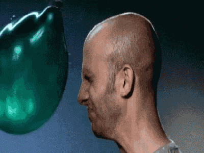 a bald man is blowing up a green balloon on his head